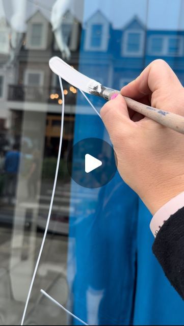 a person holding a pair of scissors in front of a window with the reflection of a building behind them