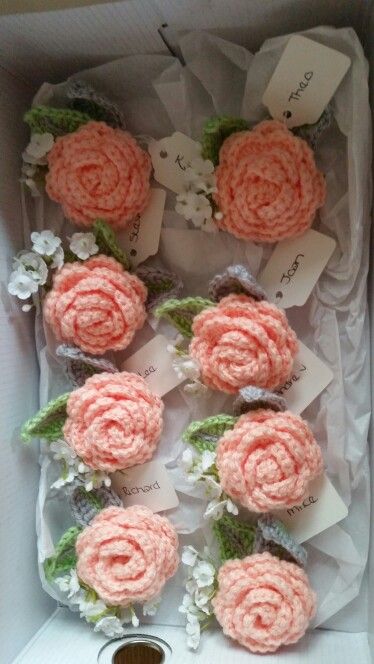 pink crocheted flowers in a white box with green leaves and tags on them