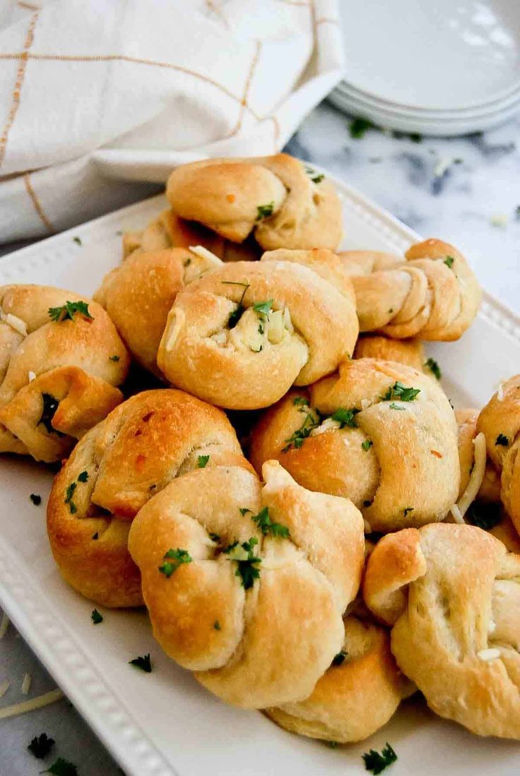 a white plate topped with rolls covered in cheese and parsley on top of a table