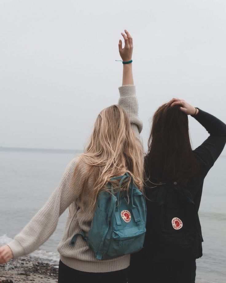 two young women standing next to each other near the ocean with their arms in the air