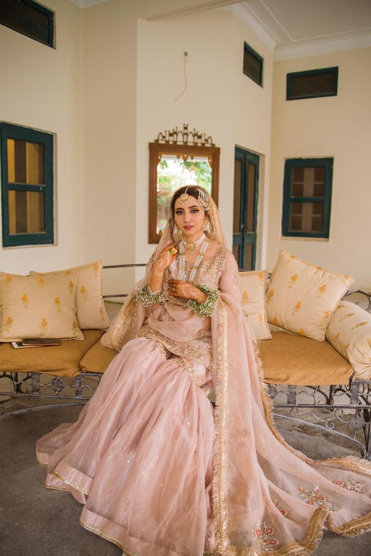 a woman in a pink lehenga sitting on a couch with her hands clasped to her face