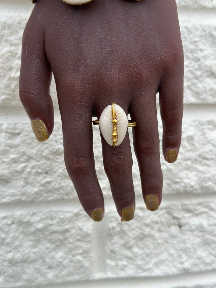 This artisanal Cowry shell and Brass adjustable Ring adds a touch of bohemian charm to any outfit. Handmade with precision and attention to detail, each ring offers a unique and stylish look. A perfect addition to your jewelry collection. sold as 1 per price Hand Wrapped Shell Jewelry, Adjustable Gold Bohemian Midi Rings, Shell-shaped Brass Jewelry For The Beach, Unique Shell Jewelry For Vacation, Bohemian Brass Jewelry For Beach, Bohemian Brass Jewelry For The Beach, Artisan Cowrie Shell Jewelry, Artisan Adjustable Cowrie Shell Jewelry, Adjustable Gold Shell Ring