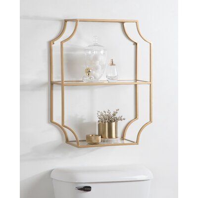 a bathroom with a white toilet and gold shelves on the wall next to it,