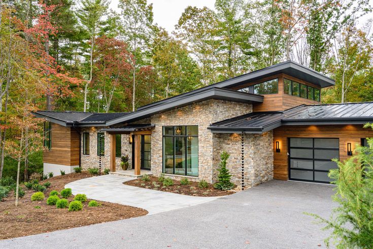 a modern home in the woods with stone and wood accents, surrounded by greenery