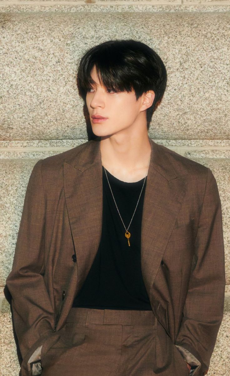 a young man in a brown suit and black shirt standing next to a stone wall