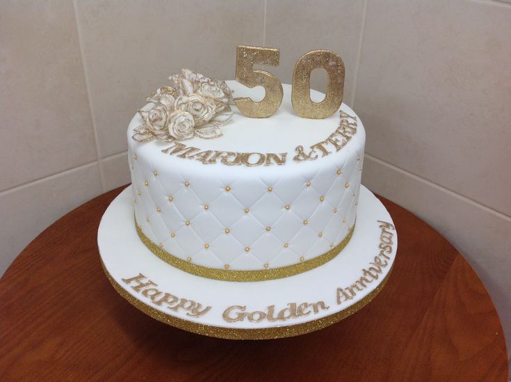 a white and gold 50th birthday cake sitting on top of a wooden table