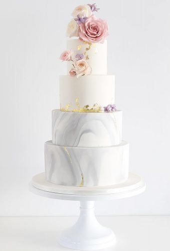 a three tiered white cake with pink flowers on top and gold flecks