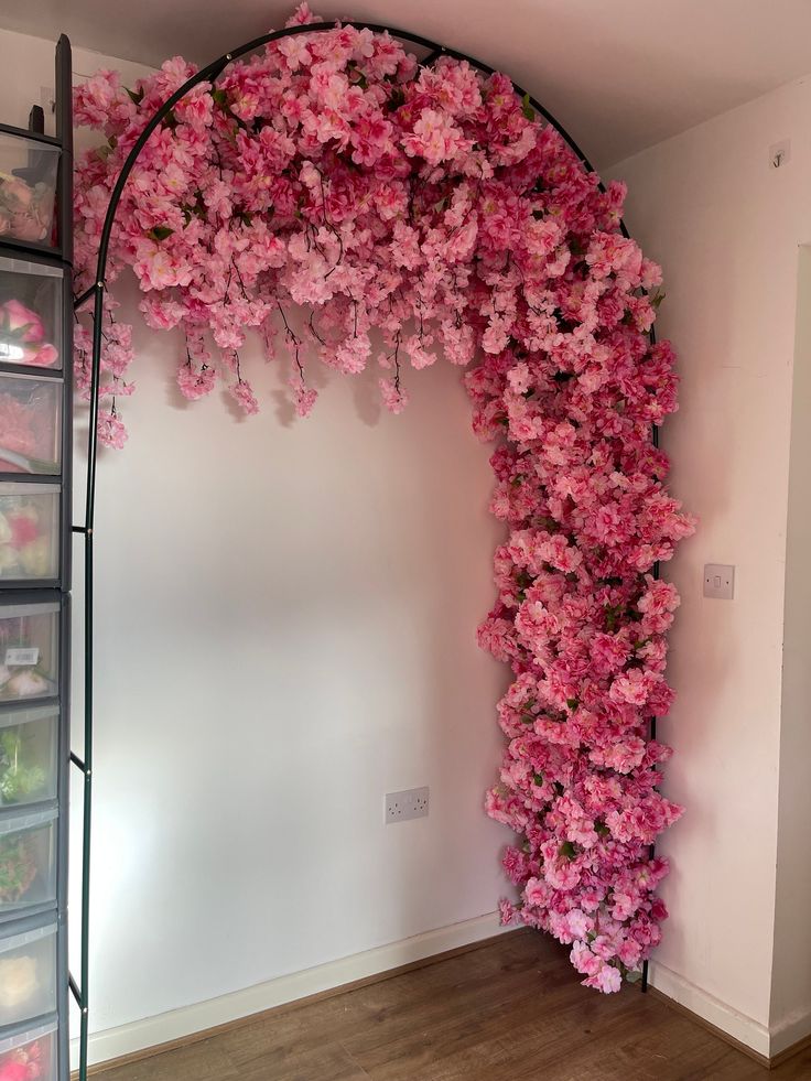 pink flowers are growing up the side of a wall in a room with clear bins