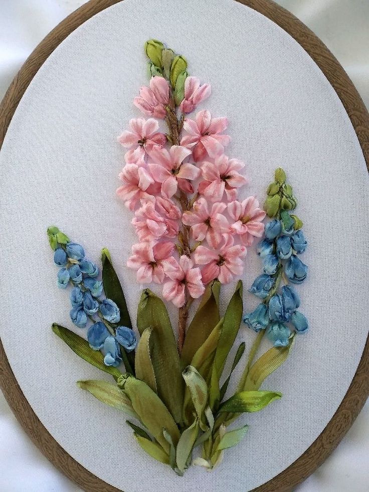 some pink and blue flowers are on a white wall hanging in a wooden circle frame