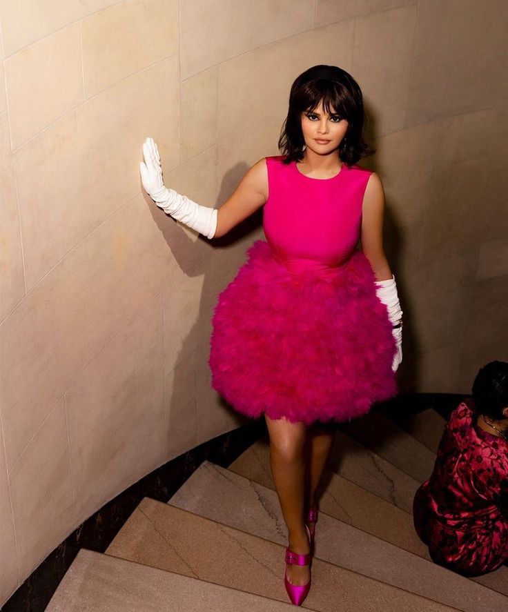 a woman in a pink dress and white gloves is standing on the stairs with her arms outstretched