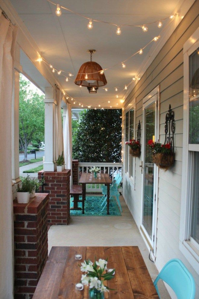 a wooden table sitting on top of a porch next to a light filled building with potted plants