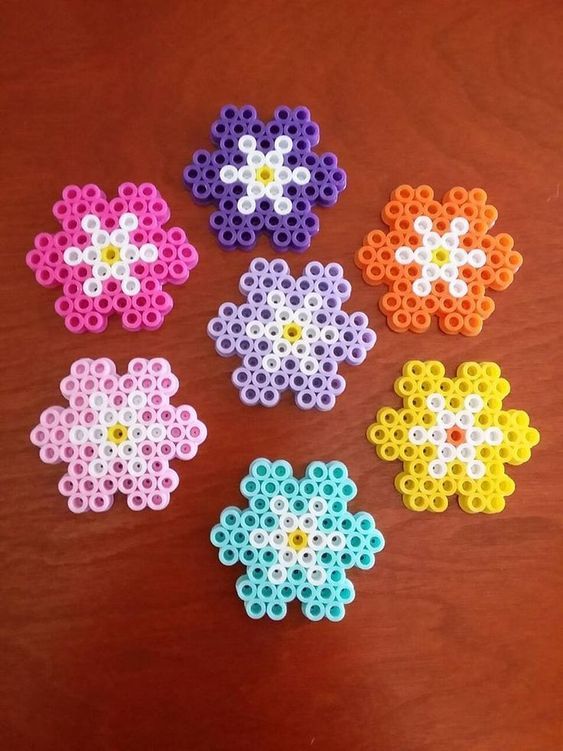 six perler beads arranged in different colors on a wooden table with one beaded flower