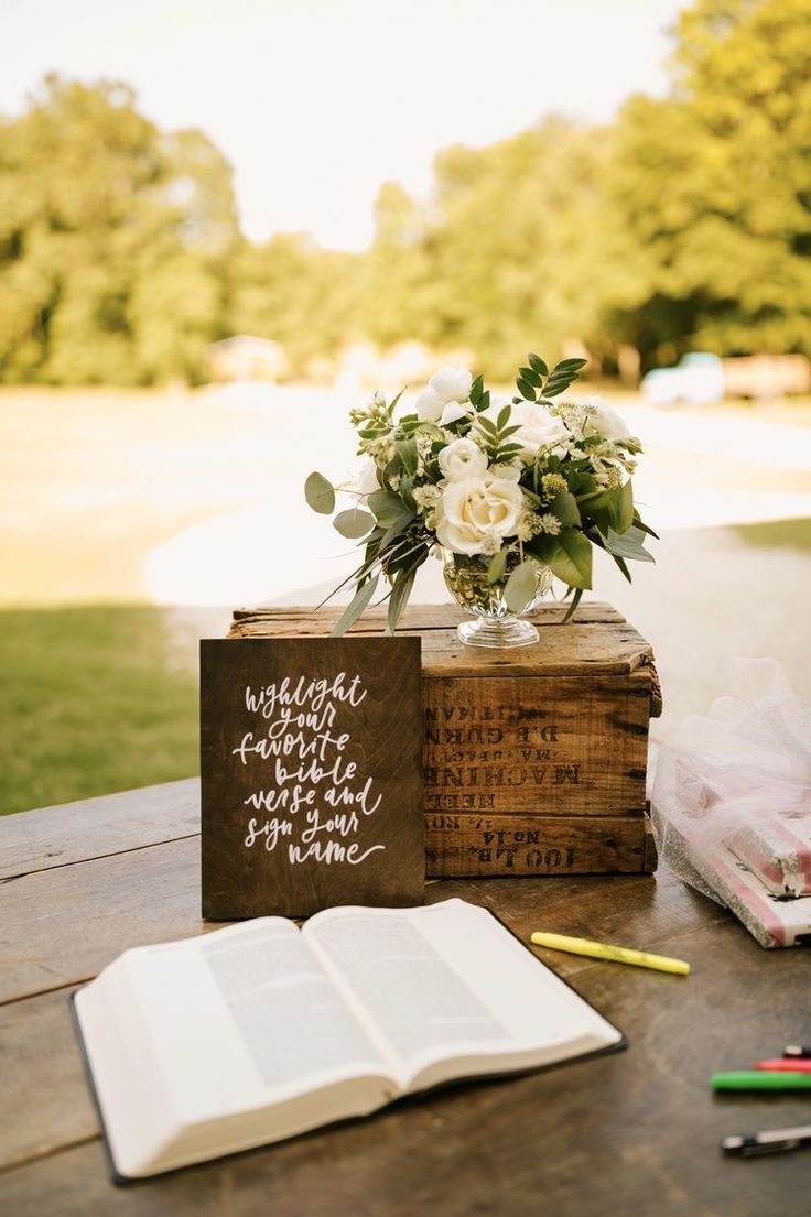 an open book sitting on top of a wooden table next to a vase with flowers