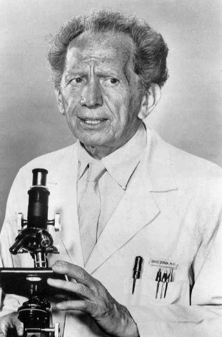 an old black and white photo of a man holding a microscope