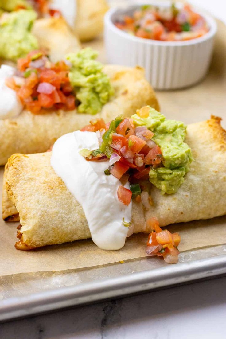 two burritos with sour cream and guacamole on top are sitting on a baking sheet