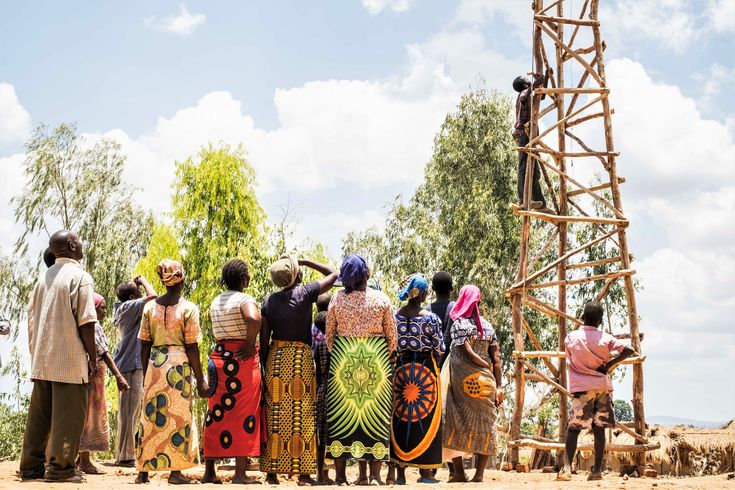 a group of people standing next to each other in front of a tall tower with a clock on it