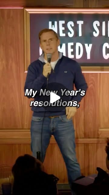 a man holding a microphone standing in front of a sign that says west side comedy club