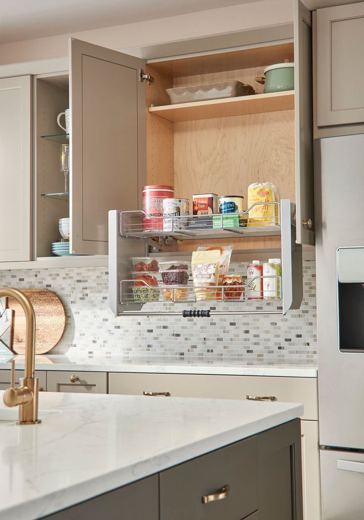 an open cabinet in the middle of a kitchen with white counter tops and gray cabinets