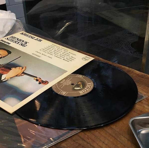 an old record player is playing music on the table next to a glass case with a sheet of paper in front of it