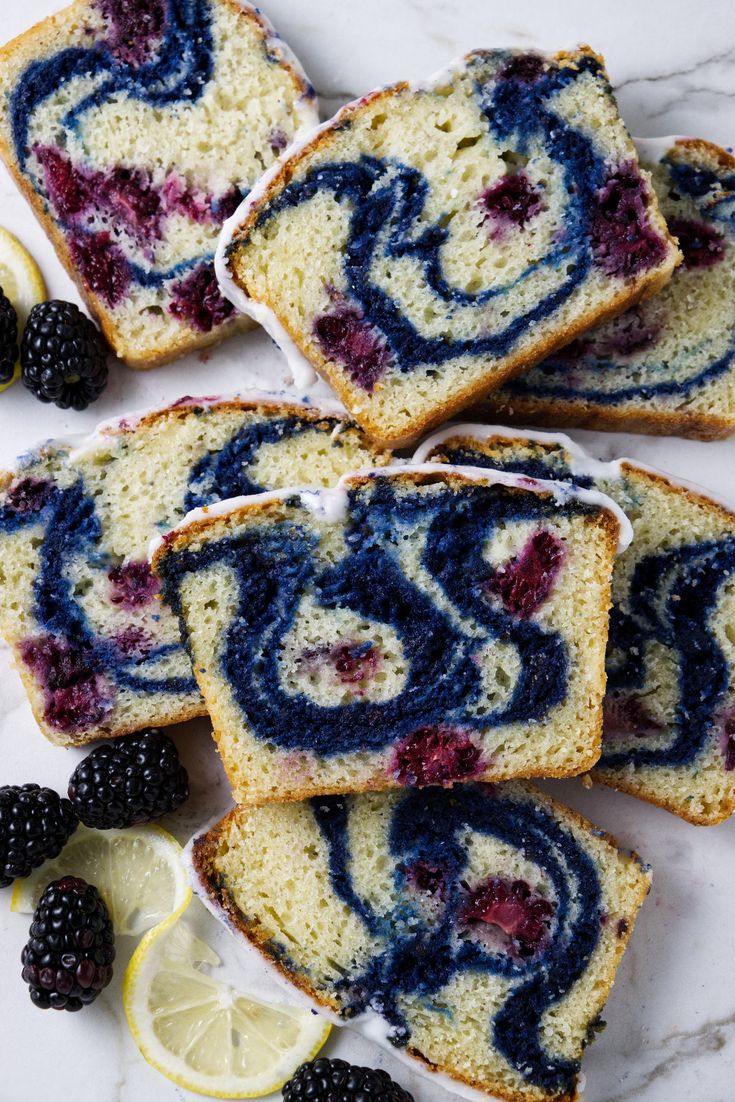 slices of blueberry swirl bread with berries and lemons around them on a marble surface