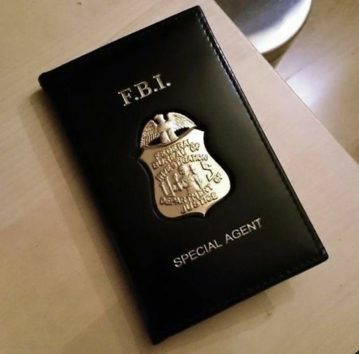 a black passport sitting on top of a wooden table next to a white plate with an emblem