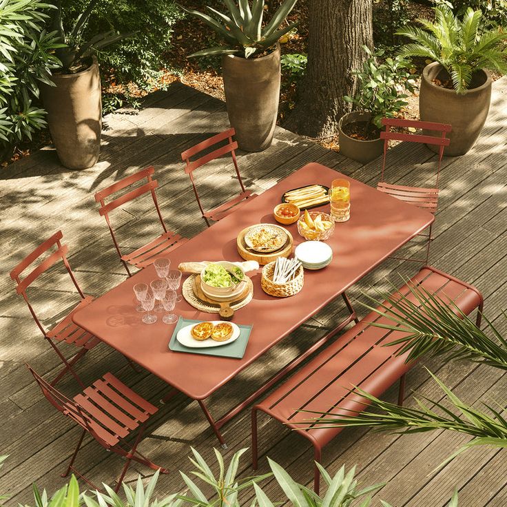 an outdoor dining table set with plates and glasses on it, surrounded by potted plants