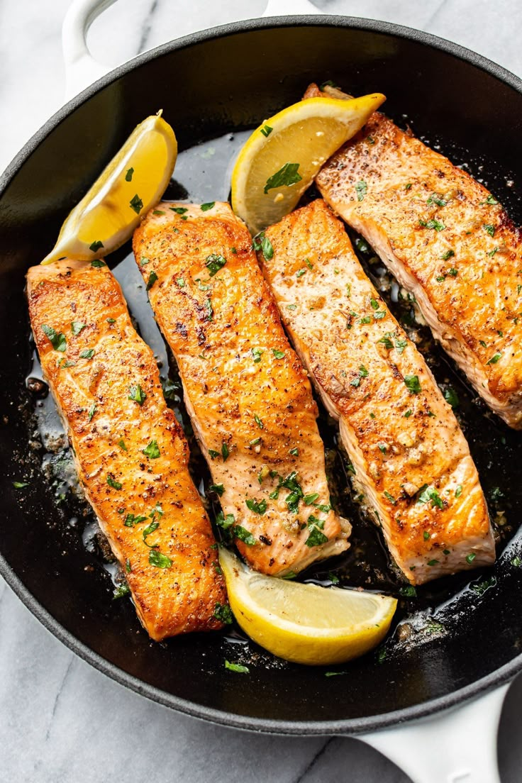 salmon in a skillet with lemon wedges and parsley