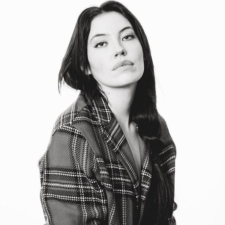 a black and white photo of a woman with long hair wearing a plaid coat, posing for the camera