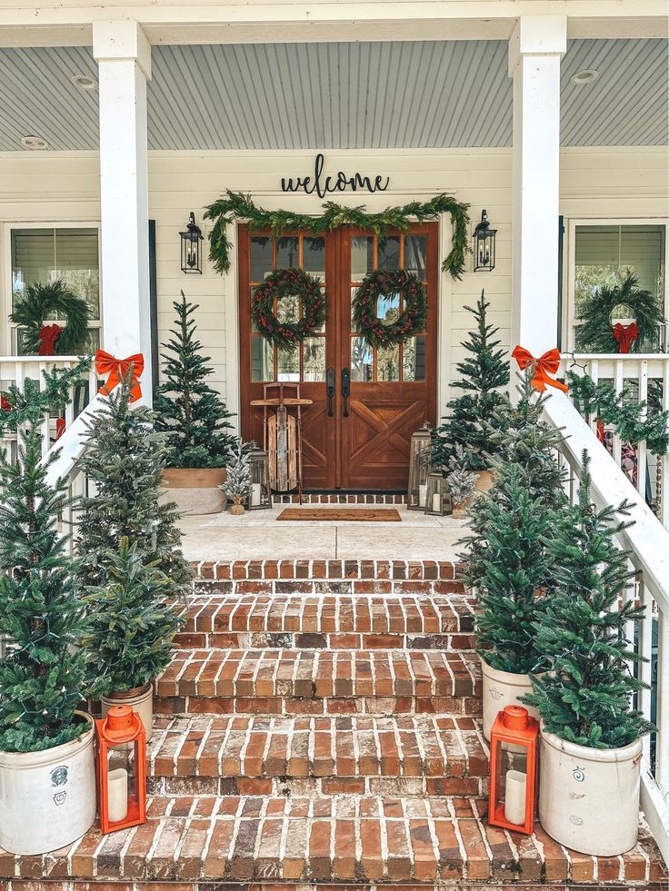 the front porch is decorated for christmas with wreaths and potted trees