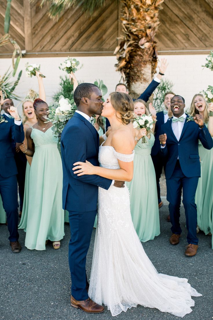 a bride and groom kissing in front of their wedding party