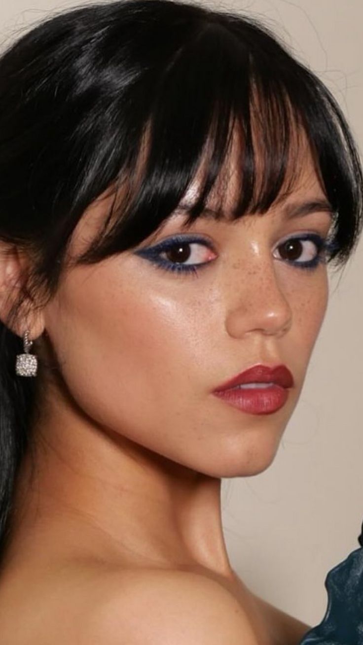 a close up of a woman with dark hair and blue eyeshadow wearing earrings