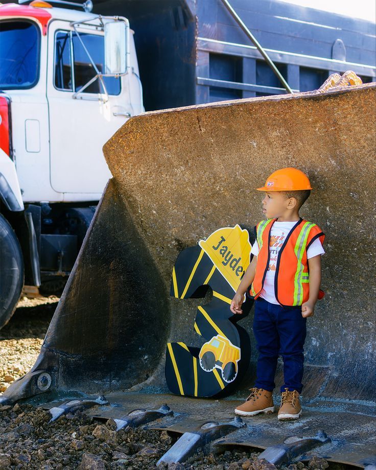 a little boy that is standing next to a big piece of construction equipment in the dirt