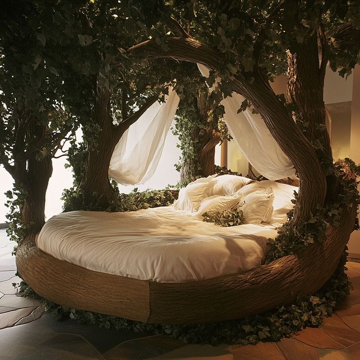 a bed made out of branches with white sheets and pillows on the bottom, surrounded by greenery