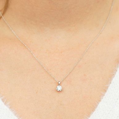 a woman wearing a necklace with a small white diamond on the front and back of her neck