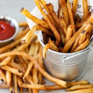 french fries with ketchup in a metal bucket on a white tablecloth next to a small bowl of ketchup