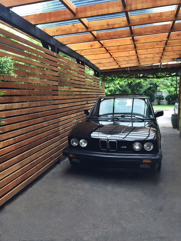 a black car is parked in front of a wooden wall with vertical slats on it