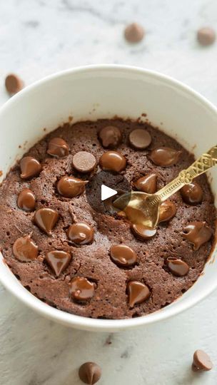 a white bowl filled with chocolate pudding on top of a marble counter next to a gold spoon