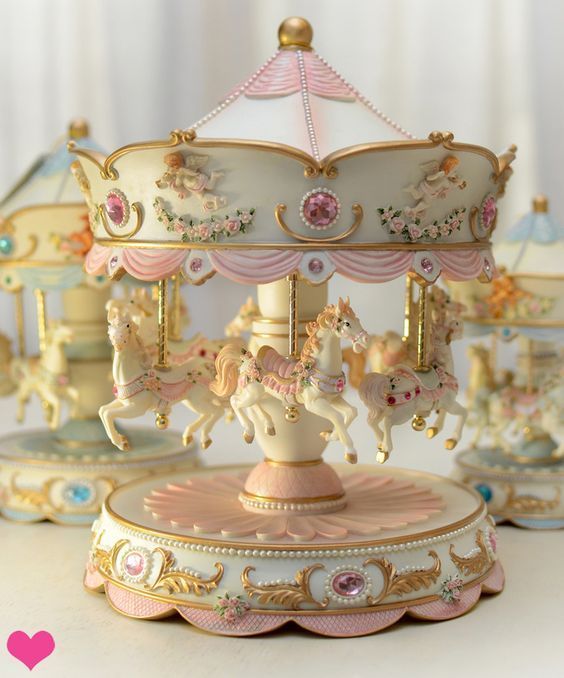 an old fashioned carousel with pink and white horses on it's top, sitting in front of other toys