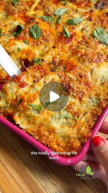 a person holding a spoon in a casserole dish with cheese and herbs on it