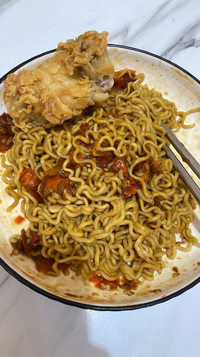 a plate full of noodles and meat with chopsticks next to it on a marble table