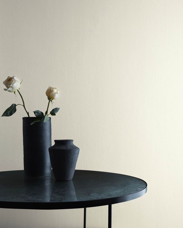 two black vases with white flowers on a table in front of a white wall