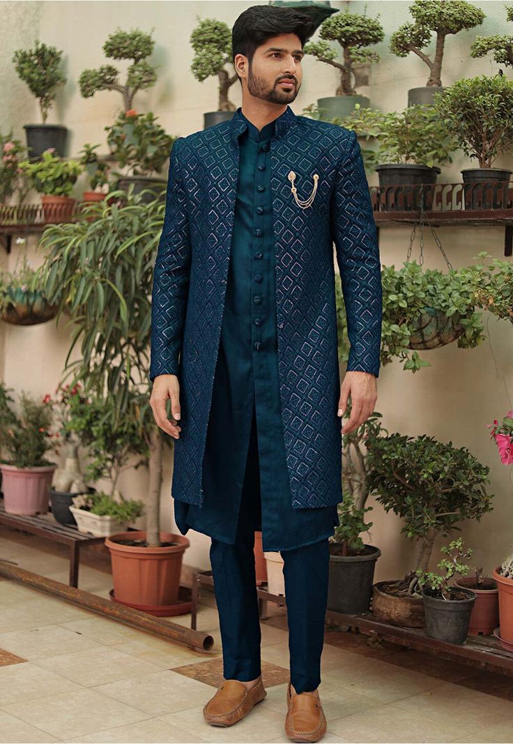 a man standing in front of potted plants wearing a blue sherve coat