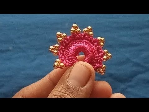 someone is holding a pink beaded brooch with gold beads in their hand and it looks like they are going to be made out of yarn