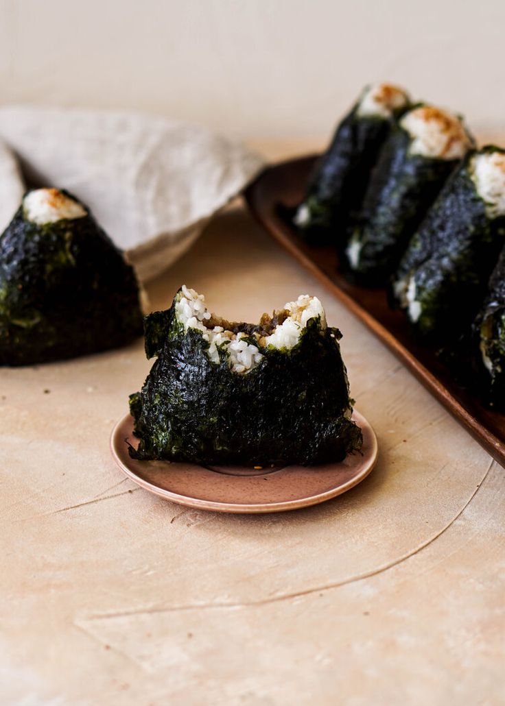 sushi rolls on a plate next to a wooden tray with white rice in it