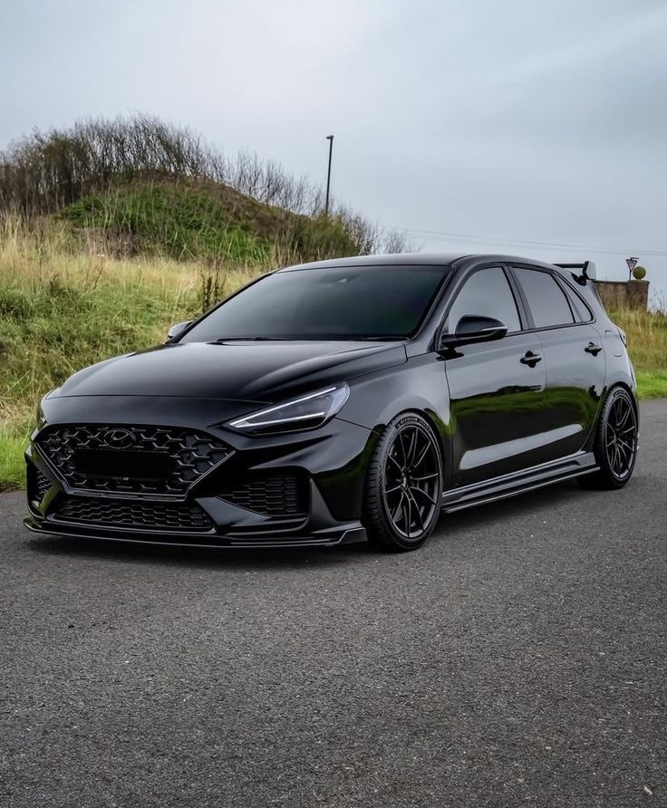 a black car is parked on the side of the road in front of some grass