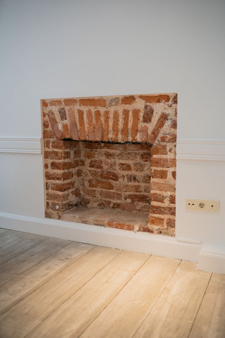 an empty room with a brick fireplace and hard wood floor