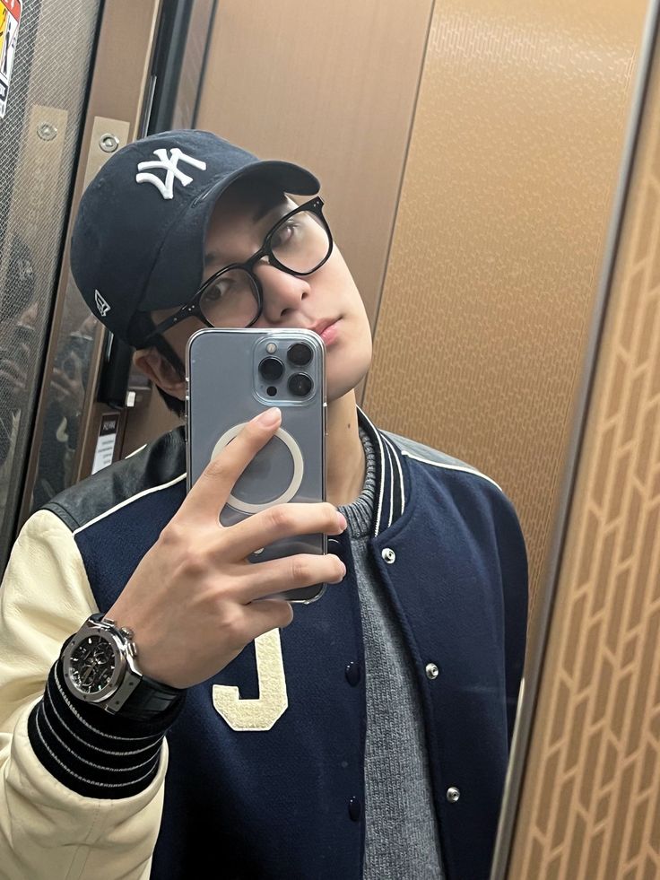 a young man taking a selfie in the mirror with his cell phone while wearing a baseball cap