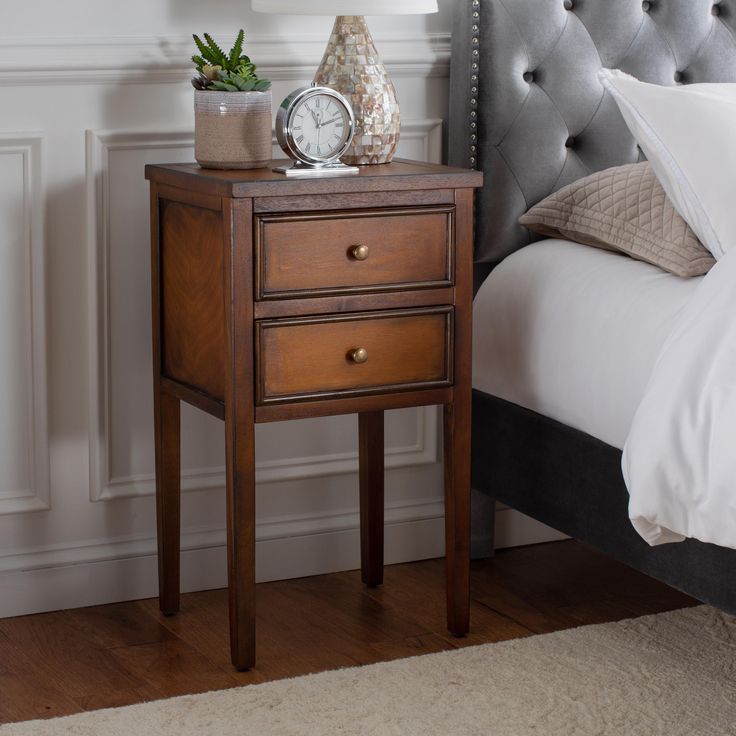 a nightstand with a clock on it next to a bed