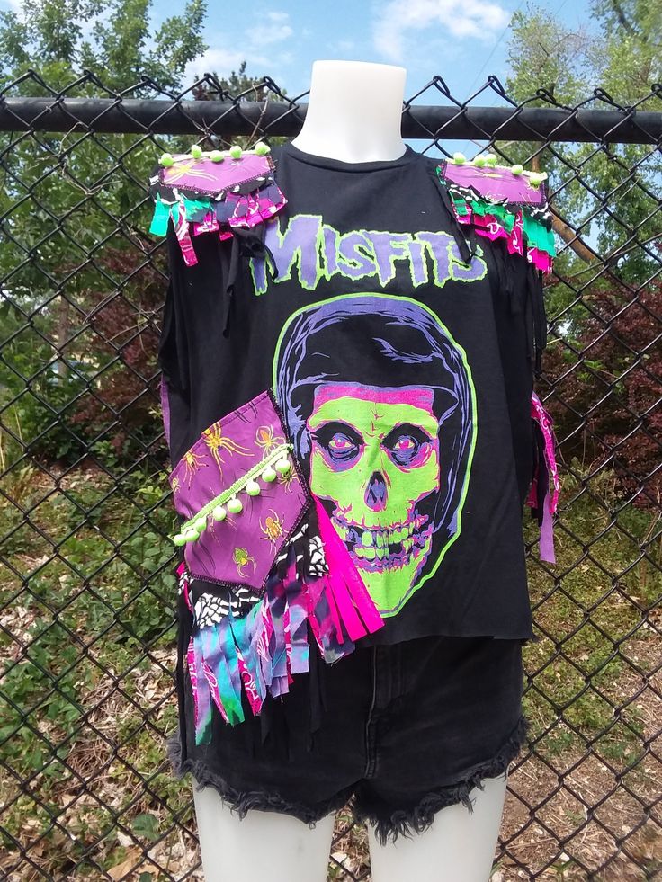 "Stay cool this summer in your new favorite shirt! Wear with your favorite shorts, pants or skirts. This shirt is made from an upcycled cropped Misfits band tee with spider print cotton broadcloth shoulder patches and pocket on the right front/side of the garment. Both are trimmed in a neon green poly pom detail and have purple and neon pink bandanna cotton broadcloth frayed fringe as well as stretch jersey fringe detail.  The back has open  fringe venting that both keeps you cool and comfortable.  Size: Mannequin is a size S but the shirt fits all the way up to a XL! See measurements. Measurements: shoulders- 36\" (18\" across front) Chest/Bust- 41\" (20.5\" pit to pit) Length from neck to hem- 19\" Pocket- 6\" Length 7\" Width  Washing instructions: Hand wash ONLY in cool water. Dry Flat Summer Skull Print T-shirt For Alternative Fashion, Skull Print T-shirt For Summer Alternative Fashion, Summer Skull Print Tops For Concert, Skull Print Tops For Concerts In Summer, Skull Print Tops For Summer Concerts, Summer Punk T-shirt For Alternative Fashion, Punk Style T-shirt For Summer, Punk Style Summer T-shirt For Alternative Fashion, Summer Punk Style Festival Tops