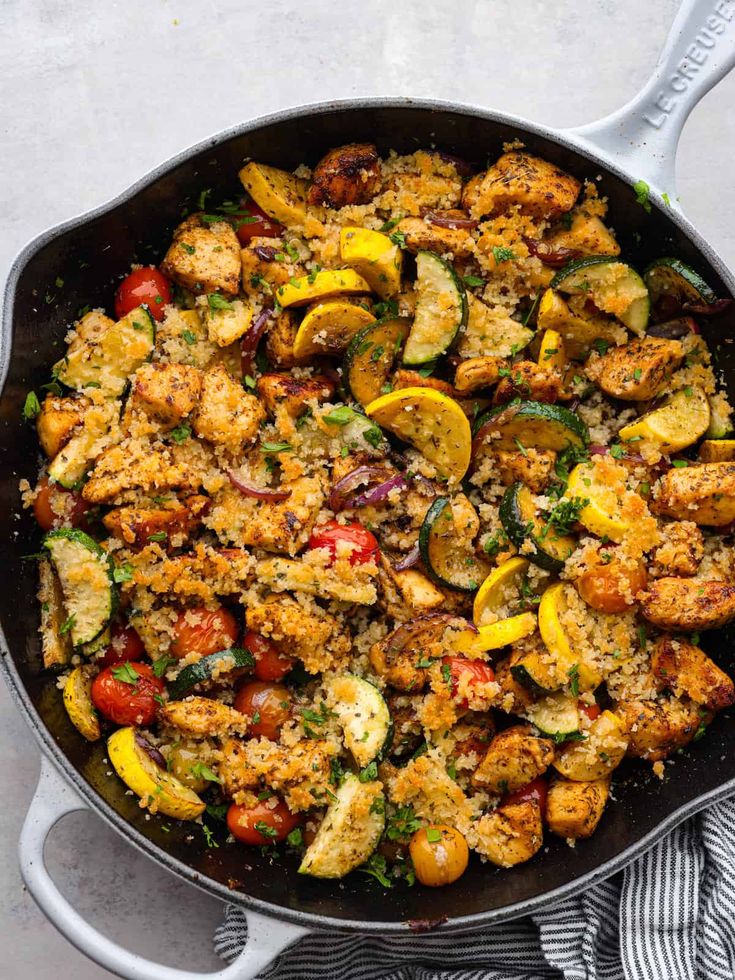 a skillet filled with chicken and vegetables on top of a table next to a towel